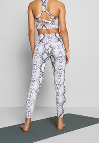 Tvådelat träningskläder set med ett orm mönster. Sports-bh:n har korslagda band och leggingsen är figurnära med ett liknande mönster.
