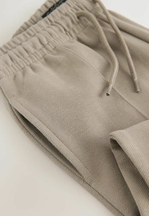 Pantalons de jogging beiges en tissu texturé, dotés d'une taille élastique avec cordon de serrage et de poches latérales.