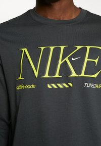 Dunkelgraues langärmeliges T-Shirt mit grünem "NIKE"-Logo, kleinem weißen Nike-Swoosh und Textakzenten "sportmode" und "TUNED AIR".