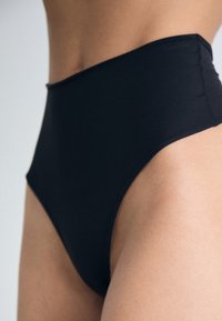 Bas de bikini noir taille haute en tissu lisse, avec un design sans coutures et une coupe qui allonge les jambes.
