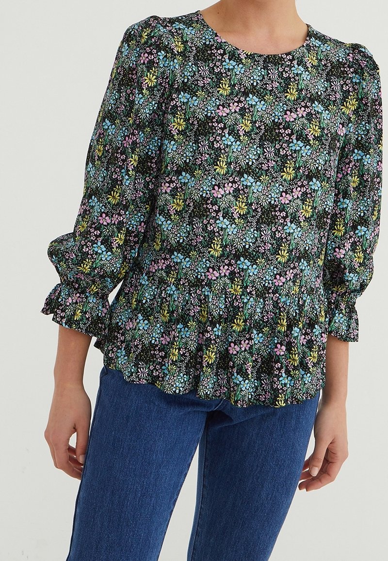 Bloemenpeplumblouse met zwarte achtergrond, voorzien van kleurrijke bloemen in roze, blauw en geel; pofmouwen en gerimpelde zoom.