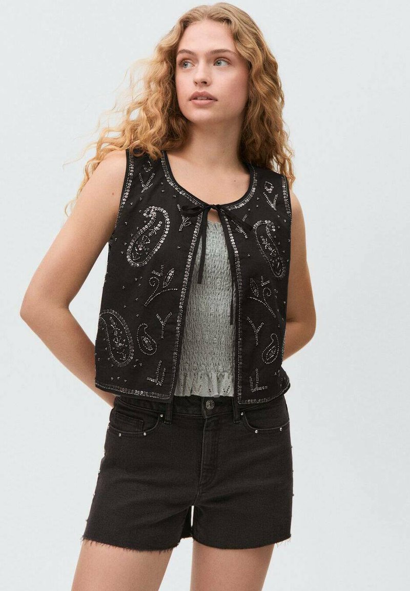 Zwart cropped vest met paisley borduursel en decoratieve kralen, gesloten met een strik. Draag het over een gestructureerde grijze top en gecombineerd met zwarte shorts.