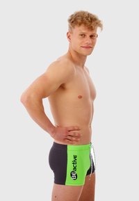 Maillots de bain pour hommes avec un schéma de couleurs noir et vert fluo. Doté d'une fermeture à cordon et d'un logo "BEactive". Design lisse et ajusté.