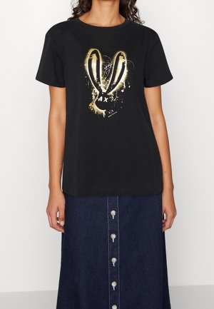 Kvinde iført sort T-shirt med korte ærmer med guld- og hvidt abstrakt kaninøre-design og mørkeblå nederdel med knapper foran.