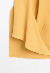 Yellow fabric with a soft drape and layered with visible stitching on a plain white background.