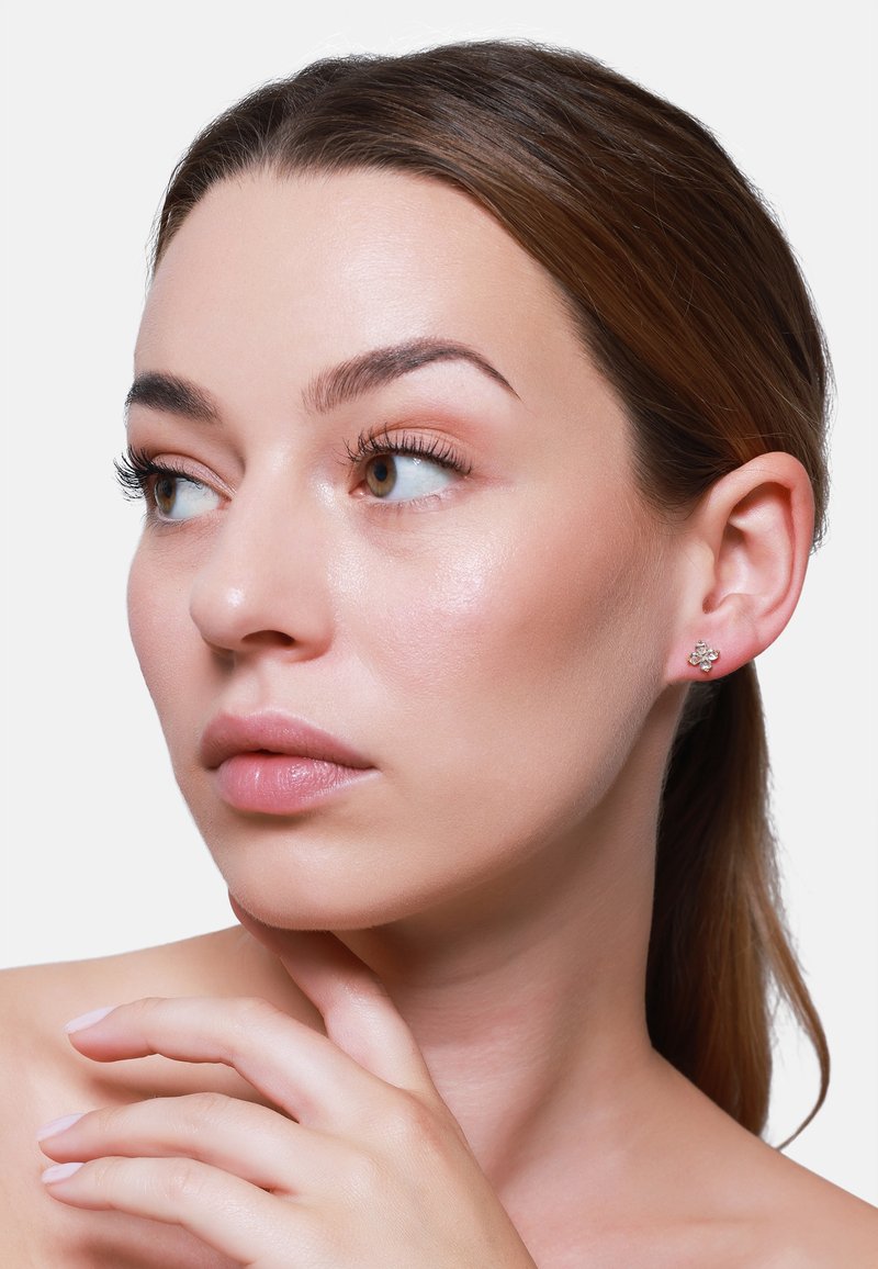 Boucle d'oreille en argent en forme de fleur, ornée de plusieurs petites pierres précieuses. Texture lisse, design délicat et éclat subtil complètent le teint de la personne qui la porte.