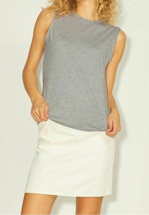 Mujer con top gris sin mangas y falda blanca, sujetando el dobladillo del top con ambas manos.