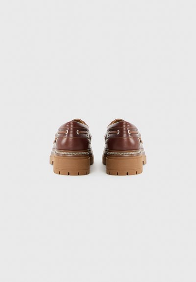 Scarpe in pelle marrone con suola spessa beige, dotate di dettagli cuciti e occhielli in metallo per i lacci. La vista posteriore mostra un design superiore liscio.