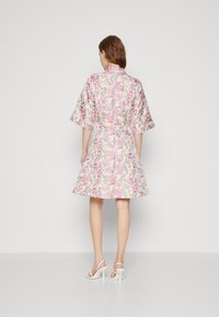 Das Blumenkleid zeichnet sich durch pinke und grüne Muster, kurze Ärmel, eine taillierte Taille und einen ausgestellten Rock aus. Es wird mit weißen, hohen Sandalen kombiniert.