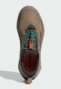 Jasnobrązowy but do wędrówek z teksturowanym cholewką, akcentami w kolorze teal i gumową podeszwą. Posiada etykietę Gore-Tex oraz elastyczny system sznurowania.