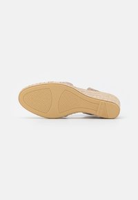 Sandalia beige con parte superior tejida, suela texturizada con un patrón antideslizante y un diseño plano, ligeramente cónico.