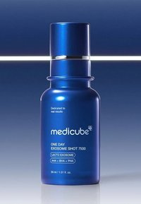 Blå glasflaska med ett silverlock, märkt "Medicube One Day Exosome Shot 7500," med produktinformation och en glänsande yta.