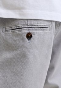 Κοντινή λήψη της πίσω τσέπης γκρι υφασμάτινου παντελονιού με σκοτεινό κουμπί και μέρος ενός λευκού πουκάμισου πάνω από την τσέπη.