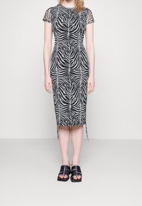 Figurbetontes Kleid mit Schwarz-Weiß-Zebra-Print, kurzen Netzärmeln, Knielänge und seitlichen Schlitzen, kombiniert mit schwarzen Riemchensandalen.