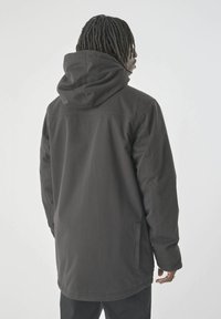 Schwarze Kapuzenjacke mit lockerer Passform, aus strukturiertem Material, mit seitlichen Taschen und geradem Saum. Die Rückansicht zeigt klare Linien und ein schlichtes Design.