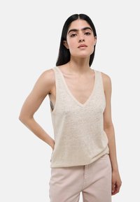 Débardeur beige à côtes avec un décolleté en V profond et des bretelles larges, associé à un pantalon rose clair. Texture douce, design décontracté et coupe ample.