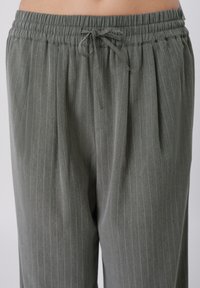 Szürke csíkos, széles szárú nadrág puha anyagból, rugalmas derékrésszel, húzózsinórral, pliszírozott részlettel és lazított fazonnal.