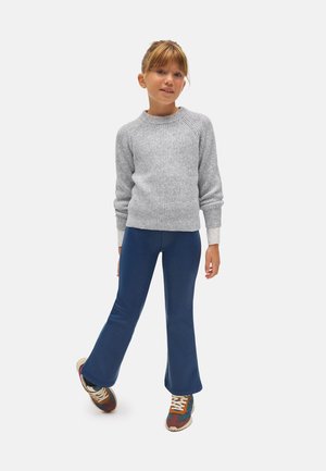 Suéter gris de punto con textura acanalada, combinado con pantalones de campana azules. La modelo lleva zapatillas de colores. Conjunto simple y casual.