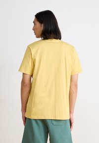 T-shirt en coton jaune à manches courtes avec un col rond, présentant une texture lisse et une coupe décontractée, vu de dos.