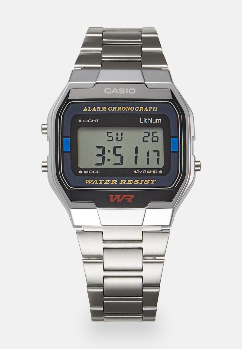 Relógio digital Casio com uma bracelete metálica prateada. Apresenta um mostrador quadrado preto, display LCD e um rótulo de resistência à água em vermelho.