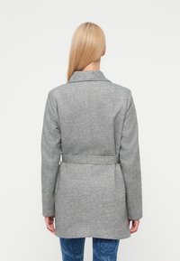 Γκρι παλτό από μάλλινο μείγμα με κολάρο ραμμένο στο σώμα, ζώνη στη μέση και μακριά μανίκια. Διαθέτει υφή υφάσματος και εφαρμοστή σιλουέτα.