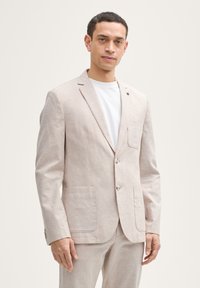 Helle beige Leinenblazer mit zwei Fronttaschen, Reverskragen und Knopfverschluss. Über einem weißen T-Shirt getragen, zeigt er eine maßgeschneiderte Passform.