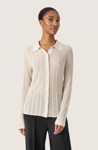 Cardigan lungo beige chiaro a maniche lunghe con colletto a punta, righe verticali e chiusura con bottoni. Realizzato in un tessuto a maglia testurizzato.