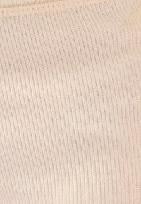 Tessuto beige a coste con una trama fine, caratterizzato da un materiale morbido e elastico. Linee orizzontali creano un pattern uniforme sulla superficie.