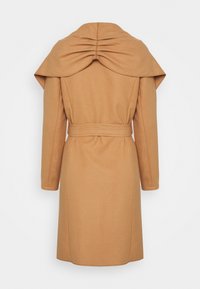 Manteau beige avec un col drapé, des manches longues et une ceinture à la taille, fabriqué dans un tissu doux et texturé, avec des détails plissés à l'arrière.