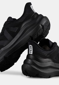Černé sportovní boty s texturovaným svrškem, kulatými podešvami a výrazným silným vzorkem. Na patě se nachází bílé logo.