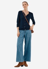 Laivastonsininen neule, napitettu, käytetty vaaleansinisten leveälahkeisten farkkujen päällä. Ruskeat nilkkurit ja ruskea olkalaukku viimeistelevät asun.