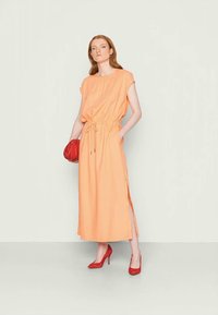 Vestido laranja até ao joelho, com um corte descontraído, fendas laterais e um cós com cordão. Combinado com uns sapatos de salto vermelhos e uma clutch a condizer.