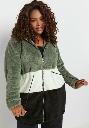 Veste en polaire zippée avec capuche en vert olive, blanc et noir. Elle présente une texture douce, des poches avant et des cordons de serrage ajustables.