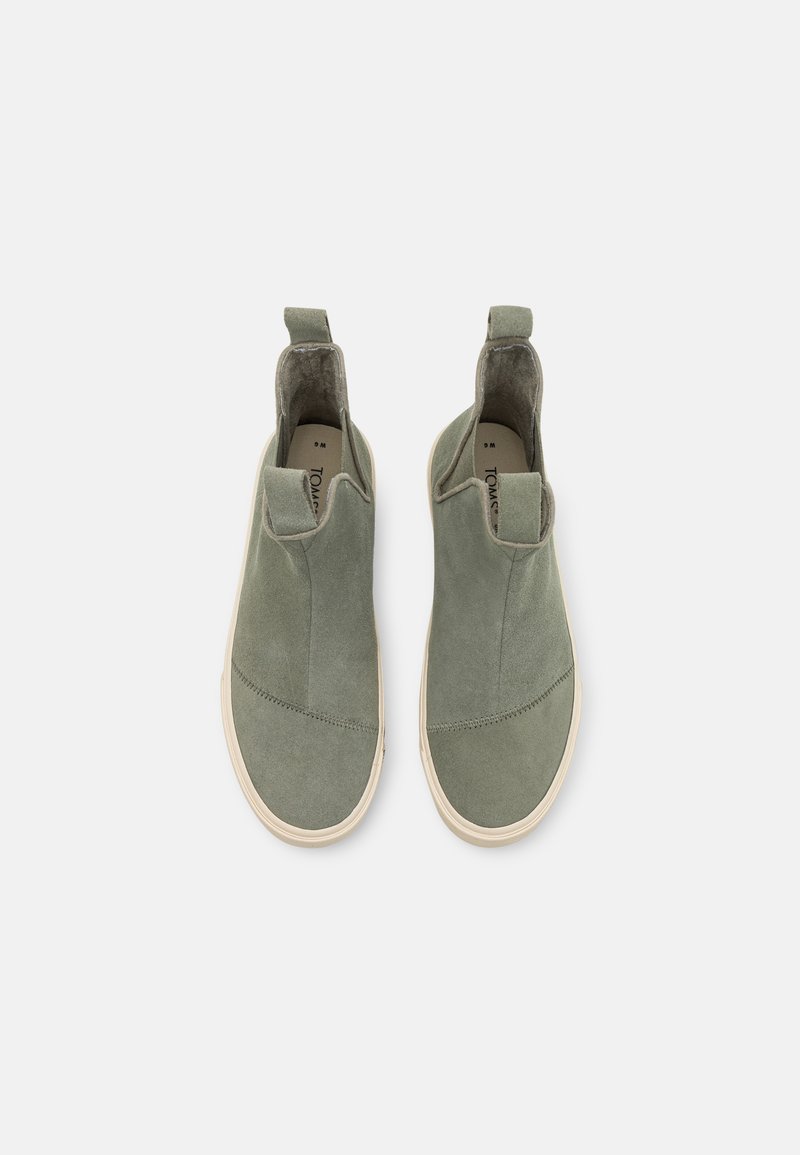 Para zielonych zamszowych botków typu slip-on kostkowych z białymi gumowymi podeszwami i uchwytami na jasnym tle, widok z góry.