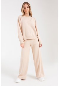 Jasno beżowy sweatshirt i szerokie spodnie wykonane z miękkiego materiału, z luźnym krojem i ściągaczami, w zestawieniu z białymi sneakersami.