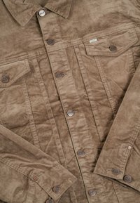 Chaqueta de pana marrón con cierre de botones, dos bolsillos frontales y cuello. Tejido texturizado con estrías visibles y botones de metal.