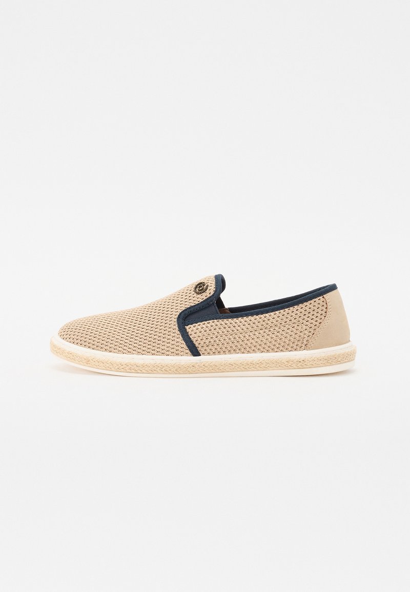 Chaussure slip-on en maille beige avec des accents bleu marine, bout rond et semelle texturée dotée de détails tressés. Design léger pour une meilleure respirabilité.