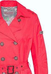 Gabardina color coral rosa hecha de tela suave, con botones dobles, cinturón en la cintura y una etiqueta de marca en la manga.