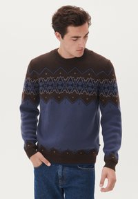 Stickad tröja i brunt och blått, med geometriska mönster och en ribbad krage. Långa ärmar med bruna mudd och nederkant.