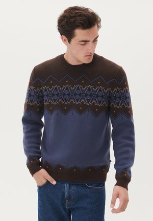 Pull en tricot marron et bleu, arborant des motifs géométriques et un col côtelé. Manches longues avec des poignets et un ourlet marron.