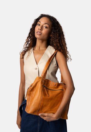 Tasche aus braunem Leder mit zwei Griffen, ausgestattet mit einer Reißverschlusstasche und Nähdetails. Die Tasche hat eine weiche Textur und ein lässiges Design.