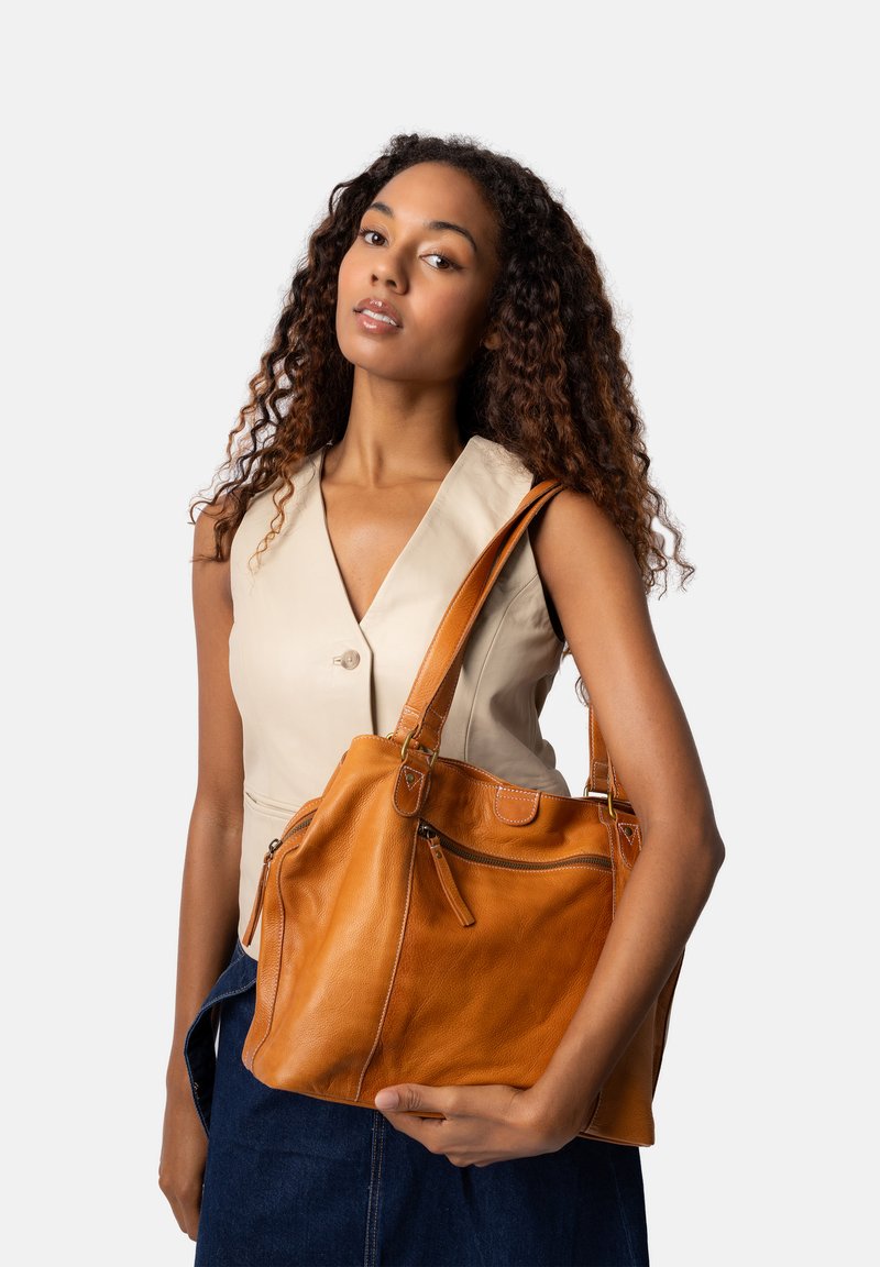 Borsa in pelle marrone chiaro con due manici, dotata di una tasca con zip e dettagli a cucitura. La borsa ha una texture morbida ed un design morbido.