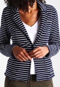 Blazer rayé bleu marine et blanc avec un col cranté, deux poches avant et une fermeture à bouton, fabriqué en tissu doux en mélange de coton.