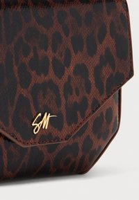 Hnědá a černá kabelka s leopardím potiskem z kůže s akcentem zlatého loga. Má geometrický design klopy a hladkou texturu.
