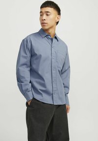 Chemise bleu clair à manches longues en coton, avec un design à boutonnières, une poche poitrine et une coupe légèrement décontractée.
