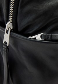 Zwarte leren rugzak met een gestructureerde afwerking. Voorzien van zilverkleurige ritsen, één zichtbaar vak met een smal riemdetail.