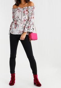 Halenka s odhalenými rameny v světle šedé barvě s růžovými a zelenými vzory, doplněná černými skinny džíny a magentovými špičatými kotníkovými botami na podpatku.