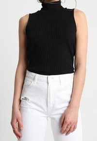 Černý žebrovaný top bez rukávů s vysokým límcem, spárovaný se sepranými bílými džíny, s přiléhavým střihem a jemnou strukturou.