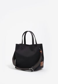 Zwarte canvas draagtas met dubbele handvatten, een afneembare bruine schouderband en een leren label. Minimalistisch ontwerp met een ruime binnenkant.