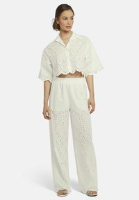 Witte katoenen tweedelige outfit met een cropped shirt van oogjeskant met geschulpte randen en wijde broek met vergelijkbare oogjesdetails.